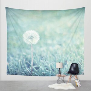 May include: A single white dandelion seed head stands tall in a field of green grass. The background is a soft, blurred blue-green color.