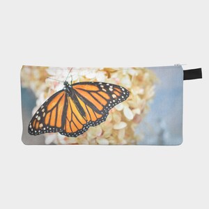 Puede incluir: Una mariposa monarca con alas naranja y negras posada sobre un grupo de flores blancas. Las alas de la mariposa están extendidas, mostrando los intrincados patrones de sus alas.