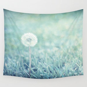 May include: A single dandelion seed head with a white, fluffy bloom stands tall in a field of soft, green grass. The background is a blurred, light blue and green color.