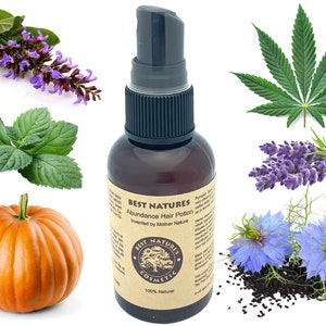 Op de afbeelding: Een bruine glazen fles met een zwarte spuitdop met het label "BEST NATURES Abundance Hair Potion" en "100% Natural". De fles is omringd door verschillende kruiden en bloemen, waaronder lavendel, munt, pompoen en zwarte komijnzaden.
