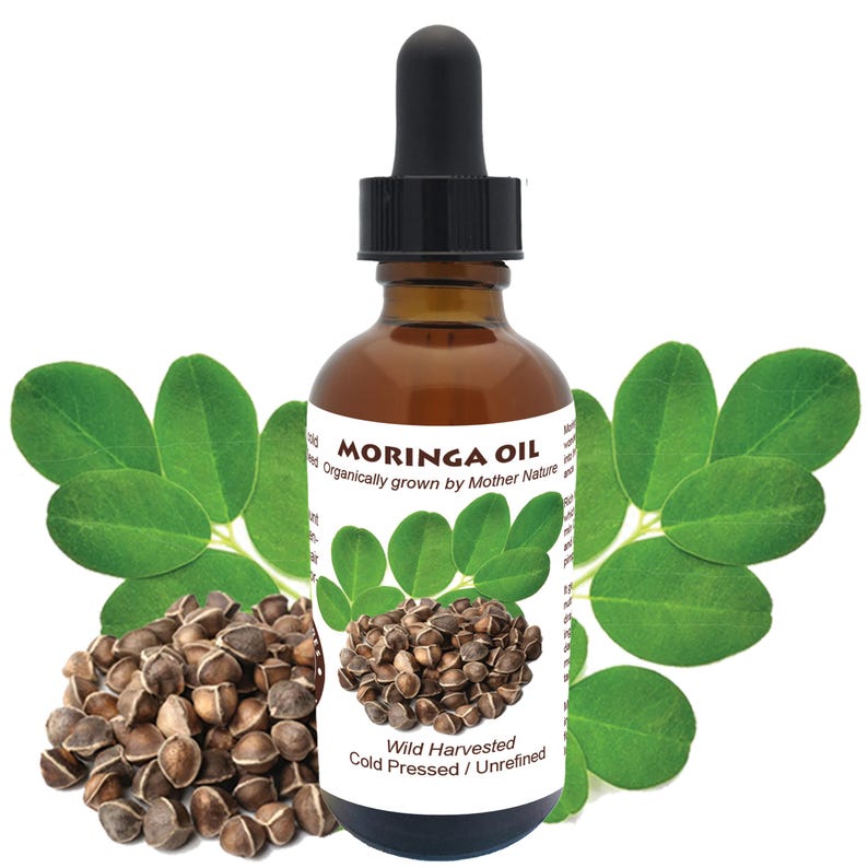 May include: A brown glass bottle of Moringa Oil with a dropper. The bottle label reads "Moringa Oil Wild Harvested Cold Pressed / Unrefined" and "Organically grown by Mother Nature". The bottle is surrounded by green leaves and brown seeds.