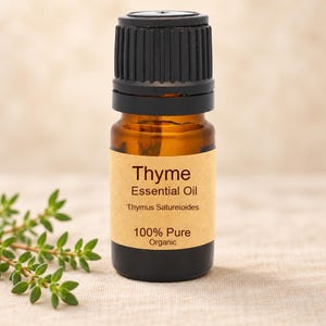 Könnte beinhalten: Eine kleine bernsteinfarbene Glasflasche mit Thymian-ätherischem Öl und einem schwarzen gerippten Verschluss. Das beigefarbene Etikett trägt den Text Thyme, Essential Oil, Thymus Satureioides, 100% Pure, Organic. Ein Zweig frischer grüner Thymian liegt daneben.