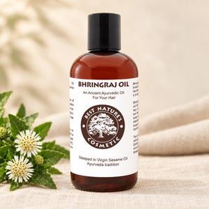 Amber bottle with black cap and white botanical label on beige cloth, bhringraj oil, Ayurvedic hair oil