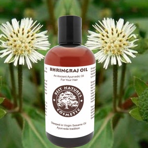 Compact amber bottle centered among green leaves and white bhringraj flowers, bhringraj hair oil, herbal scalp oil