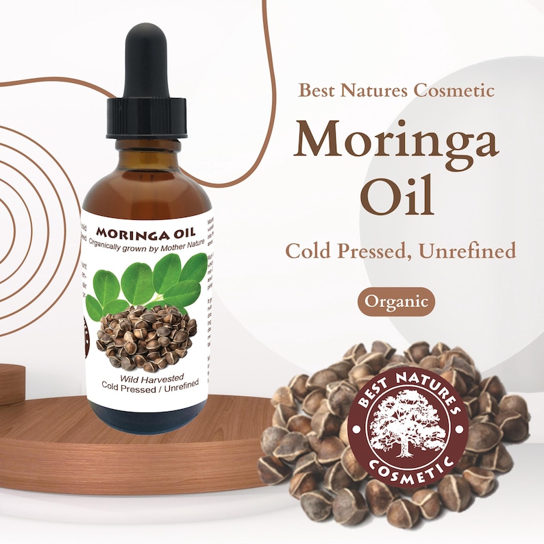 May include: A brown glass bottle of organic Moringa Oil, cold pressed and unrefined. The bottle has a white label with the words "Moringa Oil" and "Organically grown by Mother Nature" printed on it. The bottle is sitting on a wooden surface. The image also shows a pile of Moringa seeds.