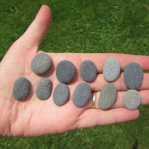 May include: A hand holding a collection of smooth, oval-shaped stones in various shades of gray.