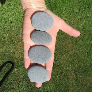 May include: Five smooth, gray stones of varying sizes are arranged in a row on a hand, with the largest stone at the top and the smallest stone at the bottom.