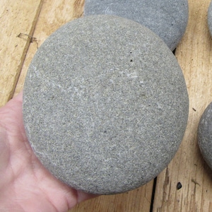 May include: A smooth, round, gray stone with a slightly textured surface. The stone is about the size of a grapefruit.