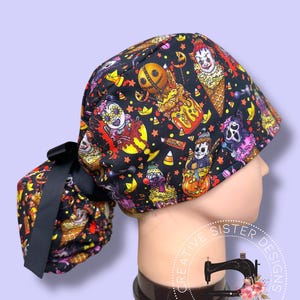 May include: Black scrub cap featuring a Halloween-themed pattern with various spooky characters, candy corn, and stars. The cap has a black bow and is designed for medical professionals. The cap is on a mannequin head.