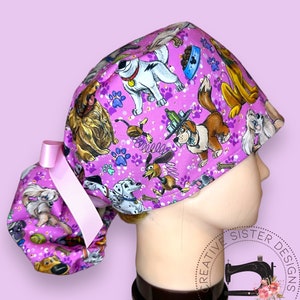 May include: A purple scrub cap featuring a playful dog-themed pattern. The cap showcases various cartoon dog illustrations, paw prints, and bone motifs. A light pink ribbon is attached to the back. The cap is designed to be worn on the head.