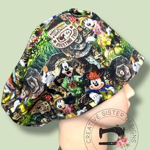 May include: A colorful scrub cap featuring a print with Mickey Mouse, Minnie Mouse, and other Disney characters. The cap has a green, brown, and black background with the text "Mickey & Friends Greeting Trails".