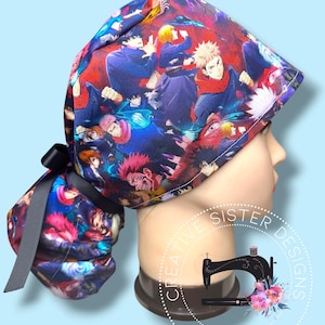 May include: A scrub cap featuring a vibrant anime character print with shades of blue, red, and purple. The cap has a gathered back section secured with a black ribbon tie. A circular logo with a sewing machine icon and the text Creative Sister Designs Handmade is visible.