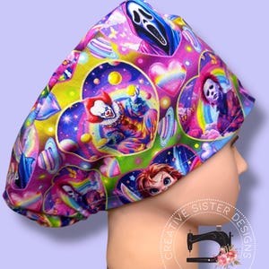 May include: A colorful surgical scrub cap featuring a vibrant pattern of horror movie characters, including a clown, a masked figure, and a ghost face. The cap is adorned with hearts, rainbows, and stars, set against a purple and blue background. The cap has the text "CREATIVE SISTER DESIGNS HANDMADE".