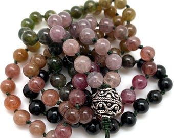 May include: A multi-colored gemstone mala necklace with a silver bead at the end. The necklace is made of green, pink, and black beads.