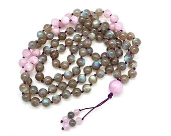 May include: A mala or prayer bead necklace made with labradorite and rose quartz beads. The necklace is strung with purple cord and has a tassel.