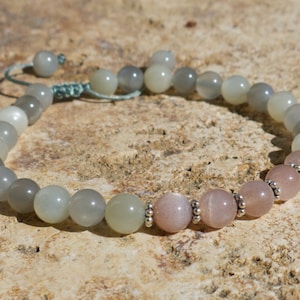 May include: A gray and pink gemstone bracelet with silver beads. The bracelet is made with round beads and has a knotted closure.