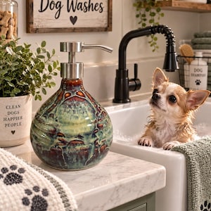 May include: A round ceramic soap dispenser with a glossy, multi-colored glaze in shades of deep blue, green, and brown, featuring a brushed metal pump mechanism. The dispenser has a wide, bulbous base that tapers toward the top.