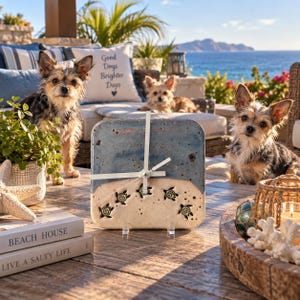 May include: A square ceramic wall clock featuring a blue and sandy beige gradient design with five small sea turtle illustrations, white clock hands, and a smooth finish, displayed on a wooden surface with books and decorative items.