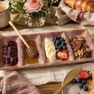 May include: A rectangular ceramic serving tray with a multi-colored glazed finish featuring four distinct sections. The tray holds red fruit preserves, golden honey with a wooden dipper, a dollop of cream, blueberries, strawberries, and pecans.
