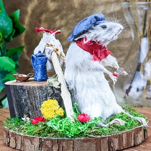 May include: A whimsical decorative piece featuring a white mouse wearing a blue hat and red scarf, holding a paintbrush. It stands on a mossy base with a miniature tea set and flowers. The base is a wood slice.