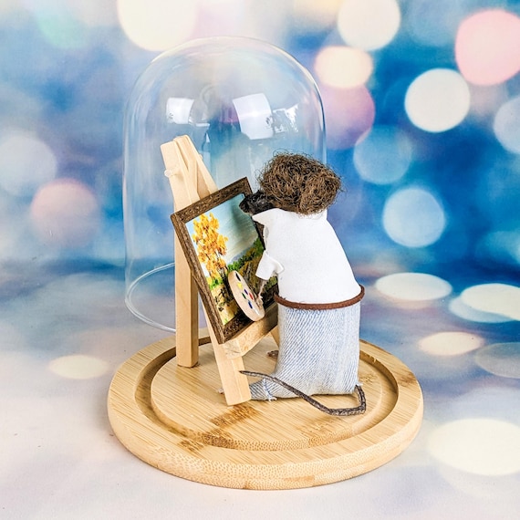 A taxidermied mouse posed as Bob Ross mid-painting session, under a glass dome — this is outsider art meets morbid whimsy at its absolute peak.