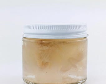 May include: A clear glass jar with a white lid filled with a translucent, light brown substance. The substance appears to be a gel or a liquid with a slightly cloudy appearance.