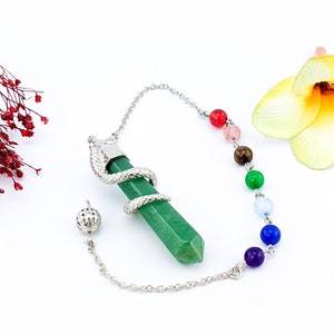 May include: A green crystal pendulum with a silver snake design wrapped around the crystal. The pendulum is attached to a chain with a series of colorful beads. The beads include red, pink, brown, green, white, blue, and purple.