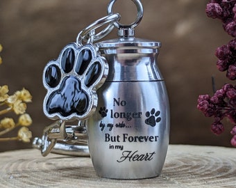 May include: A silver pet urn with a paw print charm. The urn has the words "No longer by my side... But Forever in my Heart" engraved on it. The paw print charm is black and silver.