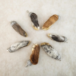 May include: A collection of six animal paw pendants arranged in a circle. Each pendant features a piece of fur in shades of brown, gray, and white, capped with a decorative silver-toned metal bail that includes a small loop for attachment.