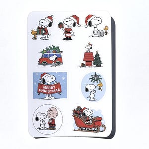 May include: A sheet of Snoopy Christmas stickers. Snoopy is shown in festive scenes, wearing a Santa hat, holding presents, and driving a red car with a Christmas tree. One sticker reads "MERRY CHRISTMAS".