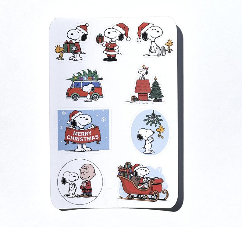 May include: A sheet of Snoopy Christmas stickers. Snoopy is shown in festive scenes, wearing a Santa hat, holding presents, and driving a red car with a Christmas tree. One sticker reads "MERRY CHRISTMAS".