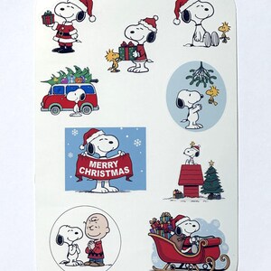 May include: A sheet of Christmas stickers featuring Snoopy and Woodstock in festive scenes. Snoopy is depicted wearing a Santa hat, delivering gifts, driving a red van with a Christmas tree, and holding a banner that reads "Merry Christmas."