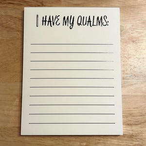 May include: A rectangular notepad with a cream-colored background featuring the black printed text I HAVE MY QUALMS: at the top. Below the text, there are ten evenly spaced horizontal black lines for writing, spanning the width of the notepad.