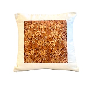 May include: Square decorative pillow with a cream-colored border and a central panel featuring a floral pattern in shades of brown and gold. The pillow has a soft, inviting appearance, suitable for home decor.