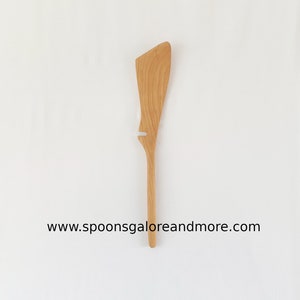 May include: A wooden spatula with a unique curved shape and a hole in the handle. The spatula is made of light brown wood and has a natural finish.