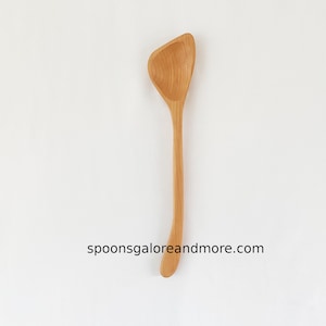 May include: A wooden spoon with a unique, curved handle and a wide, shallow bowl. The spoon is made of light-colored wood and has a natural finish.