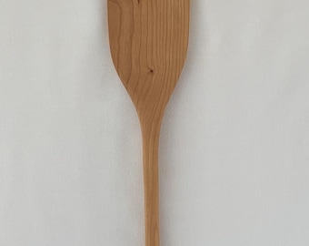 May include: A light-colored wooden spatula with a rectangular head and a long, slender handle. The spatula is made of a light-colored wood, and the grain is visible. The spatula is designed for cooking and food preparation.