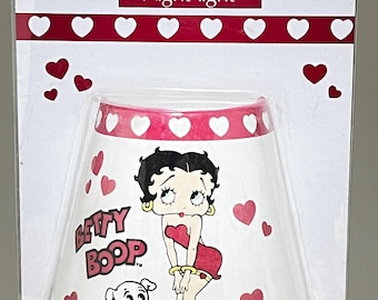 May include: Betty Boop night-light in a clear plastic package. The lamp shade is white with a red trim and heart accents. The Betty Boop character is featured on the shade, along with her dog. The packaging has the words "Betty Boop" and "Night-light".