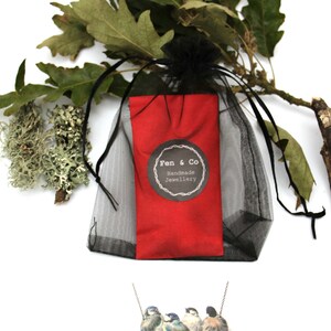 May include: A silver necklace with four bluebird charms. The necklace is packaged in a red pouch with a black mesh bag. The pouch has a black and white label that reads "Fen & Co Handmade Jewellery".
