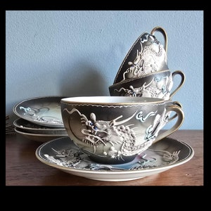 May include: A set of four black and white teacups and saucers with a dragon design. The cups and saucers are made of porcelain and have a glossy finish.