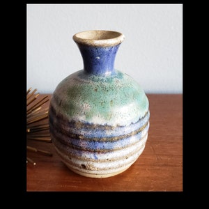 May include: A small, round ceramic vase with a blue, green, and white glaze. The vase has a narrow neck and a wide base.