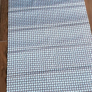 May include: A white fabric with a repeating pattern of small blue and orange paisley shapes.