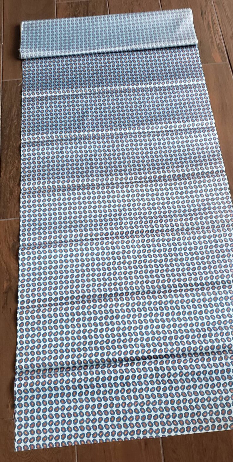 May include: A white fabric with a repeating pattern of small blue and orange paisley shapes.