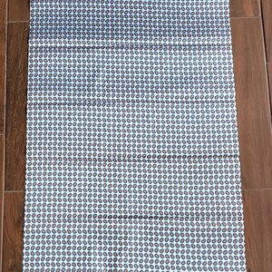 May include: White fabric with a repeating pattern of small, dark blue and orange paisley shapes.