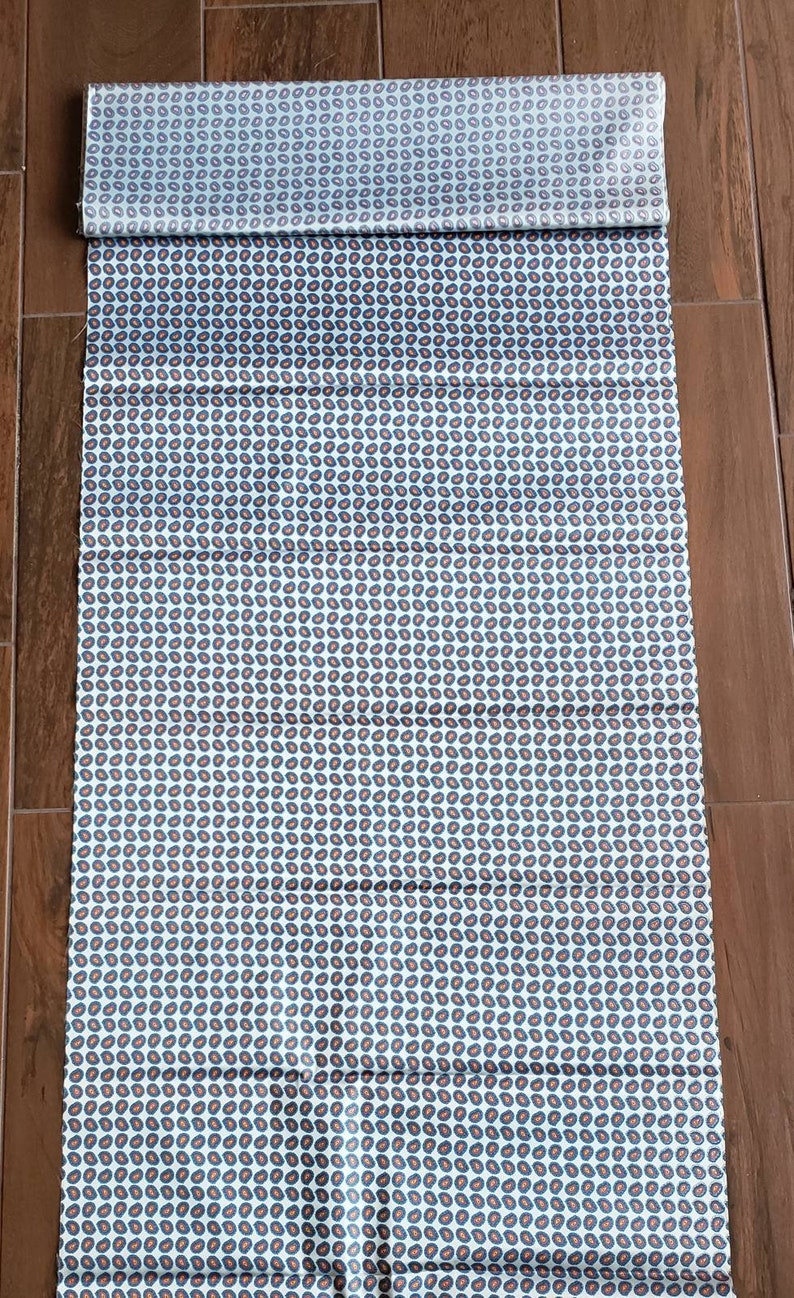 May include: White fabric with a repeating pattern of small, dark blue and orange paisley shapes.