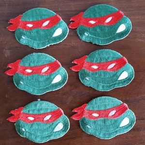 May include: Six green and red embroidered patches of Teenage Mutant Ninja Turtles' heads. Each patch features a green turtle head with a red bandana and white eyes.