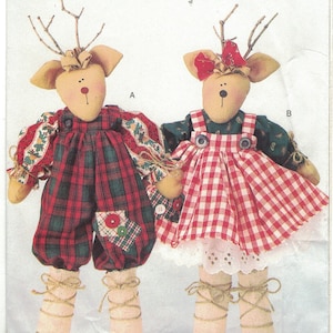 Könnte beinhalten: Ein Nähmuster für zwei Rentierpuppen. Die Puppen sind in rot-grünem Karo und rot-weißem Gingham gekleidet. Das Muster trägt den Titel "Needle in a Haystack!" und stammt von Butterick.