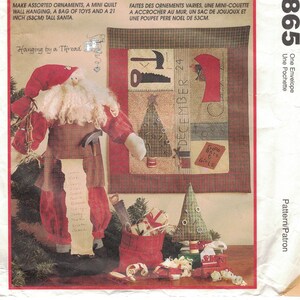 Op de afbeelding: Een vintage naaipatroon voor een kerstdeken, ornamenten en een 53 cm hoge kerstmanpop. Het patroon bevat instructies voor het maken van een tas met speelgoed en een wandhanger. De patroonhoes heeft een kleurrijke illustratie van een kerstmanpop, een kerstboom en een tas met speelgoed.