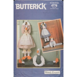May include: A Butterick sewing pattern featuring a goose and cow door stop design. The goose door stop is wearing a dress and apron. The cow door stop is wearing a dress and a shirt. The pattern is designed by Wendy Everett.