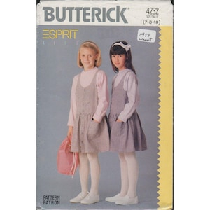 May include: A vintage Butterick sewing pattern for Esprit Kids dresses, size 7-8-10. The cover features two young girls wearing the dresses. The dresses are gray with a button-up front and pockets. The girls are wearing pink long-sleeved shirts, white tights, and white shoes.